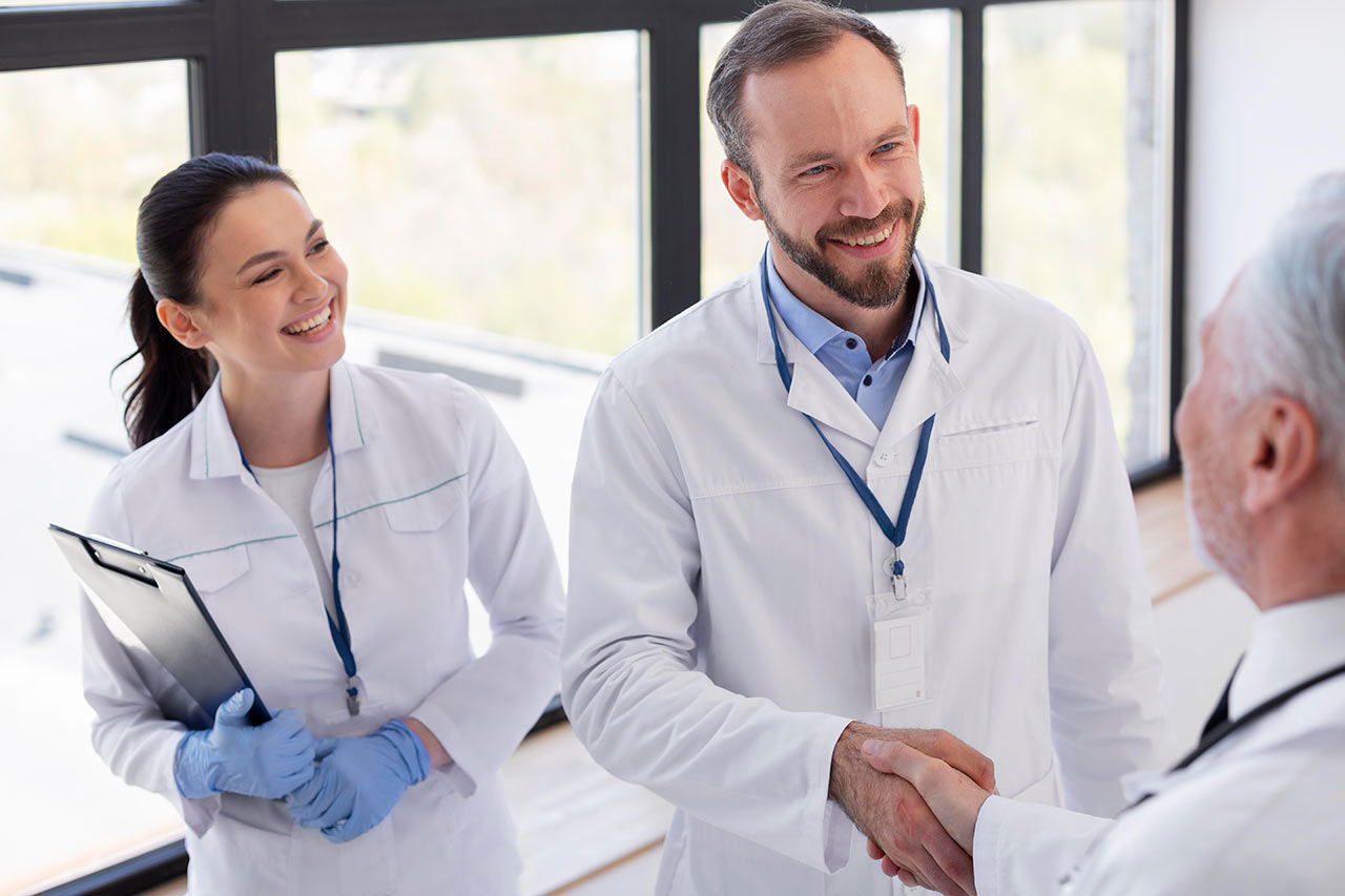 Two doctors smiling and shaking hands with a patient in a bright medical office.